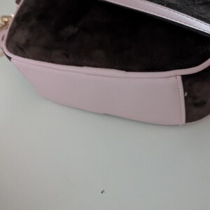 May include: A brown and pink shoulder bag with a gold chain strap. The bag has a soft, velvety texture on the top and a light pink base. The strap is a matching light pink color.