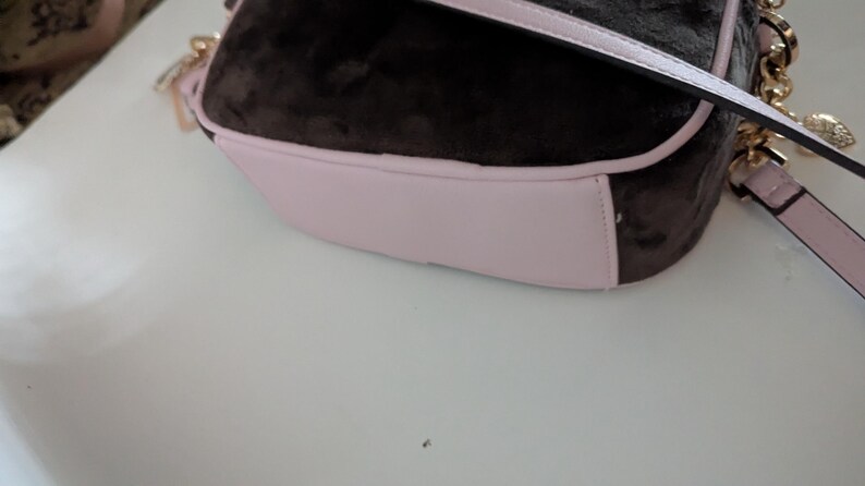 May include: A brown and pink shoulder bag with a gold chain strap. The bag has a soft, velvety texture on the top and a light pink base. The strap is a matching light pink color.