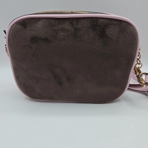May include: A brown crossbody bag with a pink trim and a gold-colored chain strap. The bag has a rectangular shape with rounded edges and a gold zipper closure. The exterior has a textured appearance.