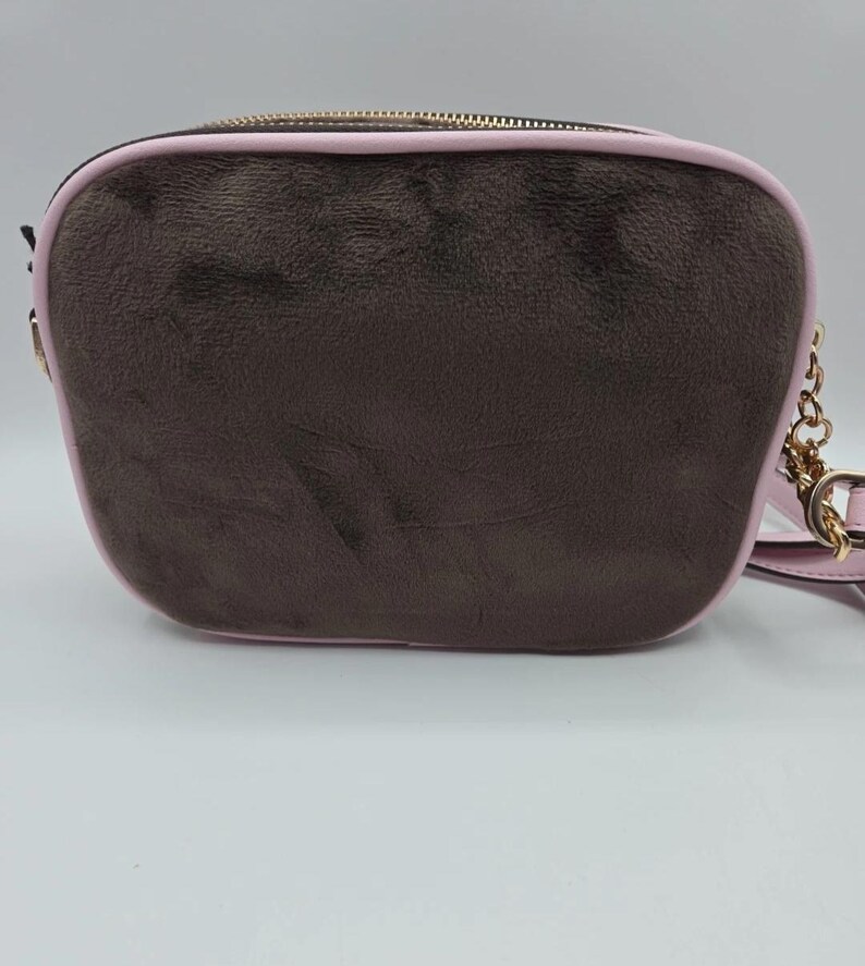May include: A brown crossbody bag with a pink trim and a gold-colored chain strap. The bag has a rectangular shape with rounded edges and a gold zipper closure. The exterior has a textured appearance.