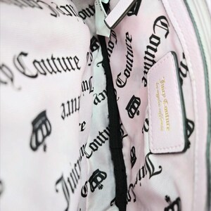 May include: Pink handbag interior with a light pink lining featuring a repeating black crown and "Couture" text pattern. A small pink leather tag reads "Juicy Couture los angeles california".