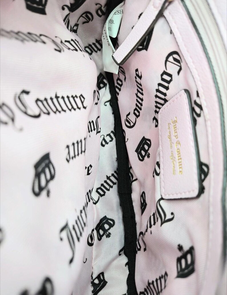 May include: Pink handbag interior with a light pink lining featuring a repeating black crown and "Couture" text pattern. A small pink leather tag reads "Juicy Couture los angeles california".