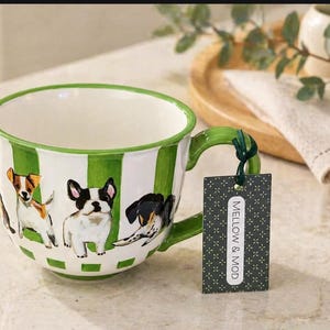 May include: A large white ceramic mug with a green handle and green and white stripes. The mug features illustrations of various dog breeds. A tag attached to the handle reads "MELLOW & MOD."