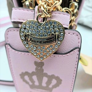 May include: A pink purse with a gold chain and a heart-shaped charm. The charm is encrusted with rhinestones and features the words "Juicy Couture." A crown design is visible on the purse.