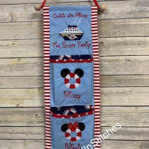 Op de afbeelding: Een blauwe stoffen wandorganizer met rood-witte gestreepte randen en een houten deuvel. Het heeft Mickey en Minnie Mouse reddingsboei ontwerpen en de tekst "Cruisin' with Mickey" en "The Scott Family".