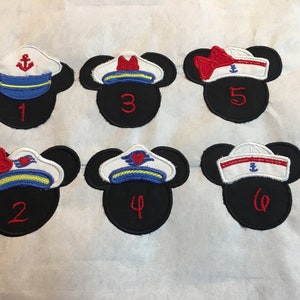 May include: Six black Mickey Mouse head-shaped patches with sailor hat designs. Each patch has a different hat design in white, red, blue, and yellow, with an anchor or heart emblem. Numbers 1-6 are embroidered in red.