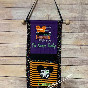 May include: A Halloween-themed wall hanging with a black hanging strap and wooden dowel. The banner features a purple top section with an orange mouse design and the text "Halloween on the High Seas". The bottom section has a black and orange striped design with a skeleton mouse.