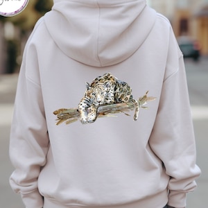 Può includere: Una felpa con cappuccio beige con un'illustrazione ad acquerello di un leopardo sdraiato su un ramo. Il leopardo è marrone, nero e bianco.