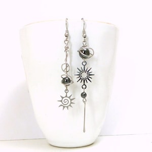 Peut inclure: Une paire de boucles d'oreilles pendantes argentées avec des perles noires et des breloques en forme d'étoile. Les boucles d'oreilles sont suspendues à une tasse blanche.