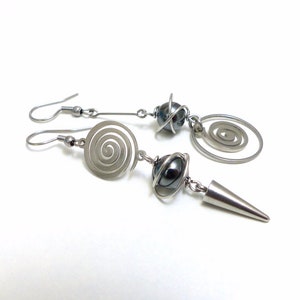 Peut inclure: Une paire de boucles d'oreilles argentées avec un motif en spirale et une perle noire. Les boucles d'oreilles sont en métal et ont un style moderne.