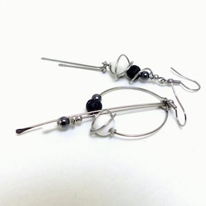 May include: A pair of modern dangle earrings. Each earring features a silver-tone metal design with a hook closure. The earrings are adorned with white and black beads, and small silver-tone beads.