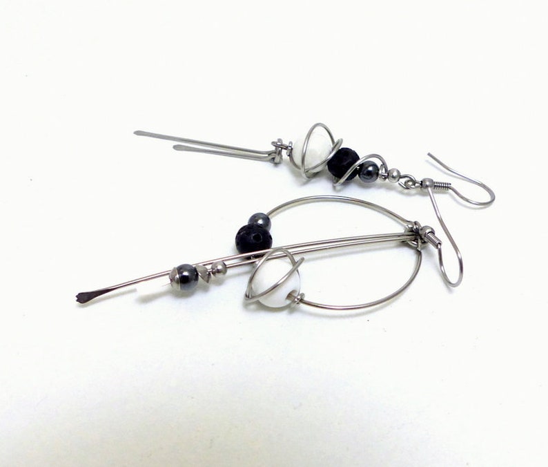 May include: A pair of modern dangle earrings. Each earring features a silver-tone metal design with a hook closure. The earrings are adorned with white and black beads, and small silver-tone beads.