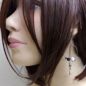 May include: Silver-tone dangle earrings with a circular design. The earrings feature black and white beads, and small silver accents. The earrings are hanging from a mannequin's ear, showcasing the jewelry's design and style.