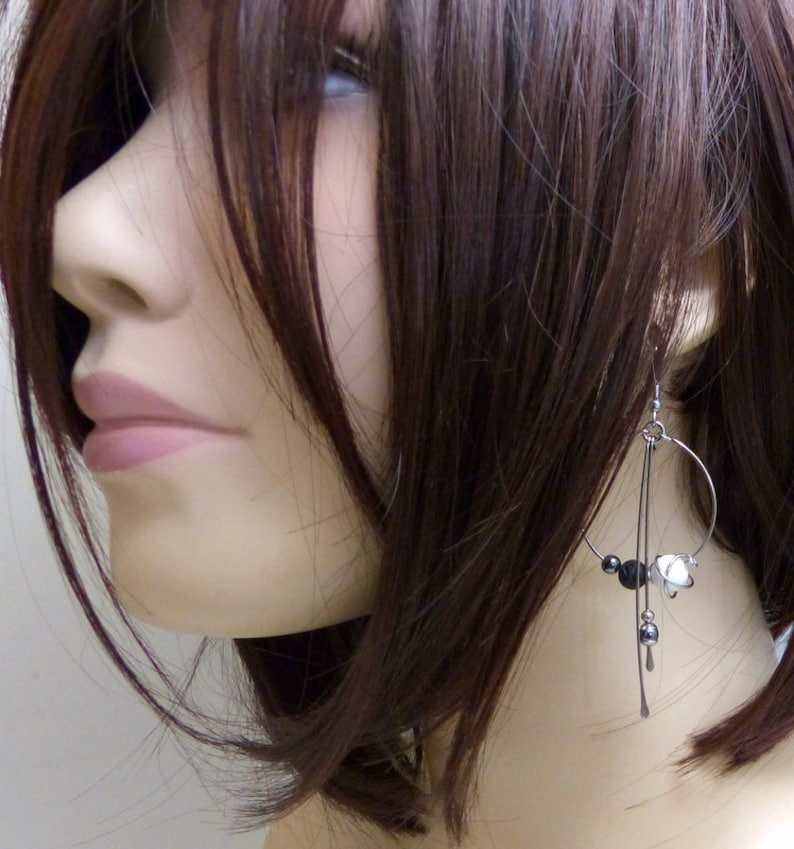May include: Silver-tone dangle earrings with a circular design. The earrings feature black and white beads, and small silver accents. The earrings are hanging from a mannequin's ear, showcasing the jewelry's design and style.
