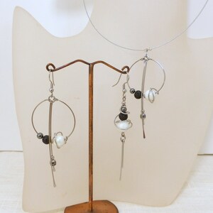 May include: A silver-toned wire jewelry set featuring a necklace and earrings. The earrings and necklace have a circular design with white and black beads. The jewelry is displayed on a mannequin bust.