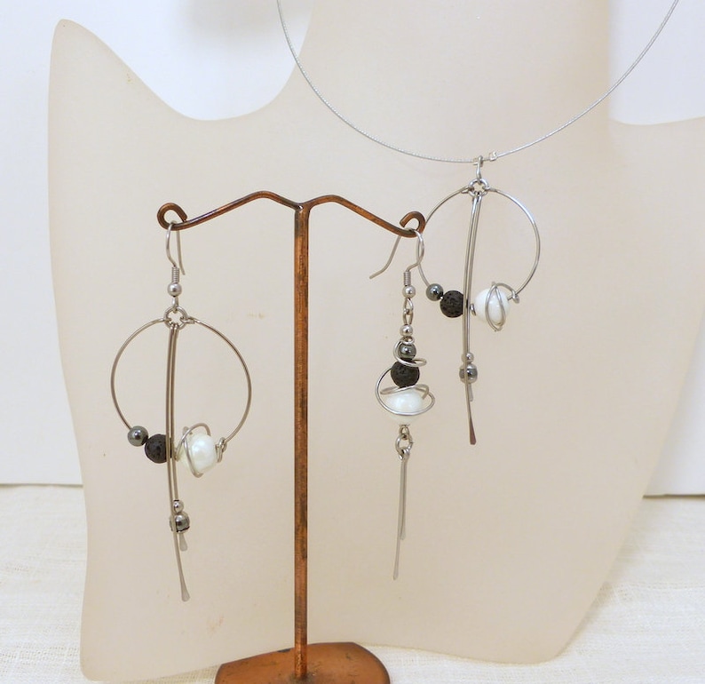 May include: A silver-toned wire jewelry set featuring a necklace and earrings. The earrings and necklace have a circular design with white and black beads. The jewelry is displayed on a mannequin bust.