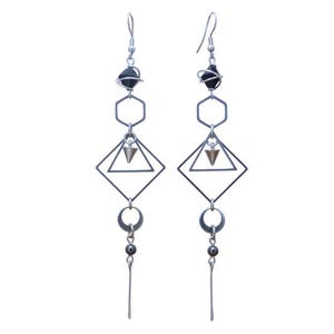 Peut inclure: Une paire de longues boucles d'oreilles argentées avec des formes géométriques, dont un hexagone, un diamant et un triangle. Les boucles d'oreilles présentent une perle noire en haut et une perle argentée en bas.