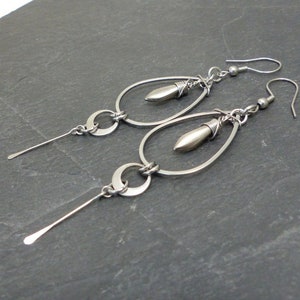 Può includere: Un paio di orecchini pendenti in argento con forma a goccia e una piccola perla d'argento in fondo. Gli orecchini hanno un design semplice e moderno.