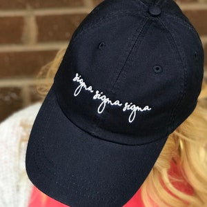 Puede incluir: Una gorra de béisbol negra con texto bordado en blanco que dice "sigma sigma sigma".