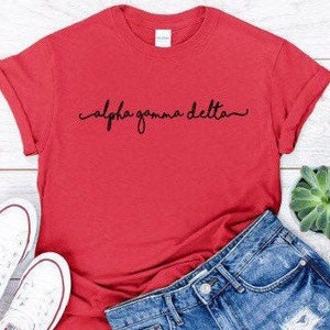Puede incluir: Camiseta roja con un diseño de escritura cursiva negra que dice "alpha gamma delta"