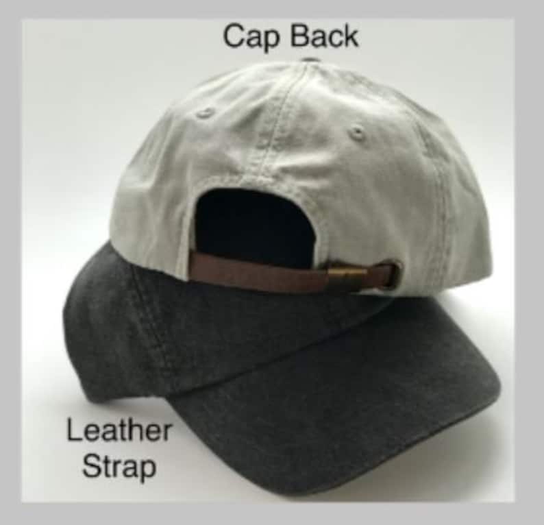 Puede incluir: Una gorra de b&eacute;isbol gris y negra con una correa de cuero y una hebilla de metal. La parte posterior de la gorra dice "Cap Back" y la correa dice "Leather Strap".
