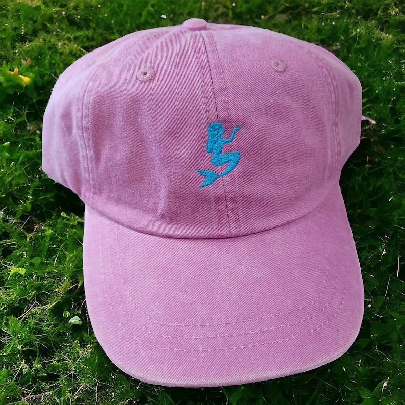 Puede incluir: Una gorra de b&eacute;isbol rosa con un dise&ntilde;o de sirena bordado en azul.