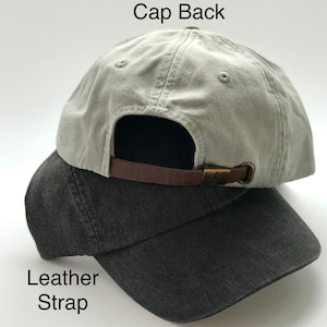 May include: A gray baseball cap with a brown leather strap and a brass buckle. The cap is shown from the back. The strap is labeled "Leather Strap". The back of the cap is labeled "Cap Back".