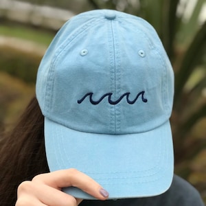 May include: A light blue baseball cap with a navy blue wave embroidered on the front.