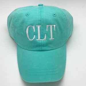 May include: A turquoise blue baseball cap with white embroidered letters spelling "CLT" on the front.
