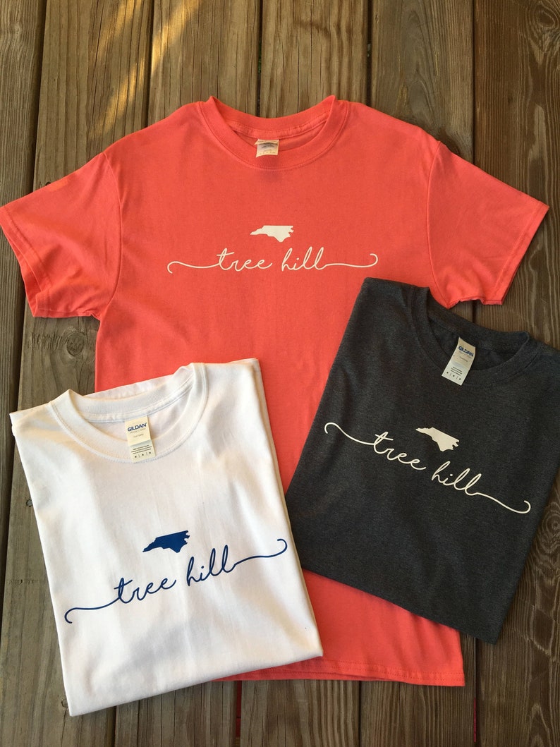May include: Three t-shirts with the text "tree hill" and an outline of the state of North Carolina. The shirts are in coral, white, and dark grey.