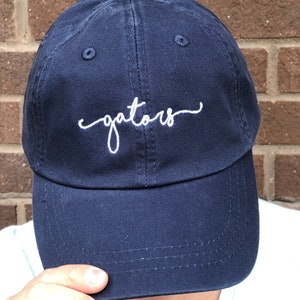 May include: A navy blue baseball cap with white embroidered text that reads "gators".
