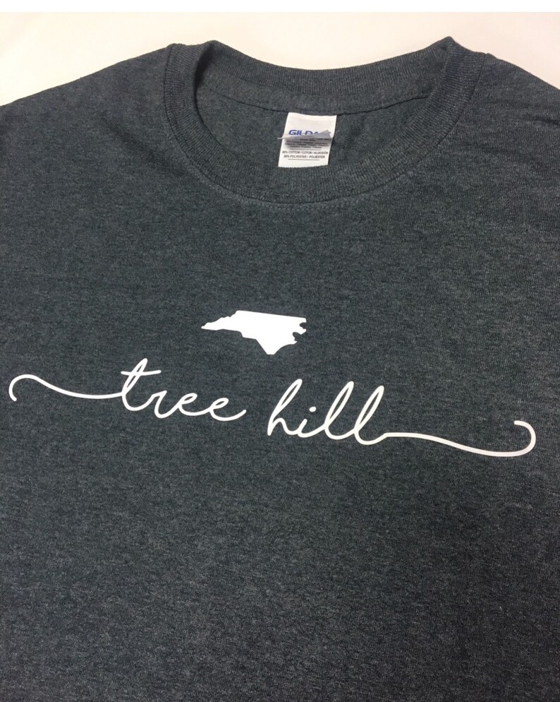 May include: A dark gray t-shirt with a white outline of the state of North Carolina and the text "tree hill" in white cursive.