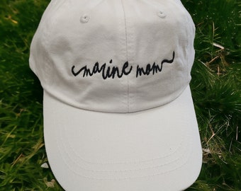 May include: White baseball cap with black embroidered text that reads "marine mom".