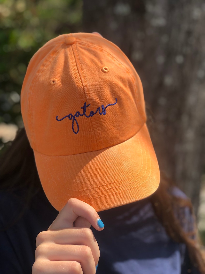 K&ouml;nnte beinhalten: Orangefarbene Baseballkappe mit dem Wort "gators" in Blau auf der Vorderseite gestickt.