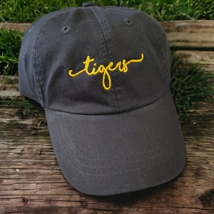 May include: A dark gray baseball cap with a yellow embroidered cursive word "tigers" on the front.