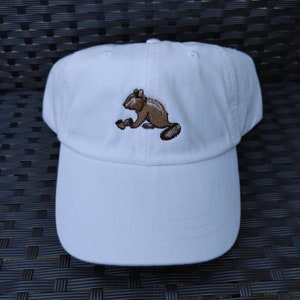 Peut inclure: Casquette de baseball blanche avec un écureuil brodé en brun.