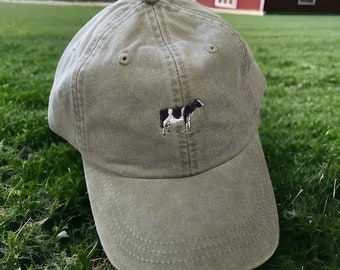 May include: A green baseball cap with a black and white cow embroidered on the front.