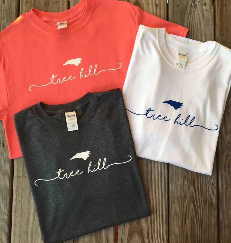 May include: Three t-shirts with the text "tree hill" and an outline of the state of North Carolina. The shirts are in coral, white, and dark grey.