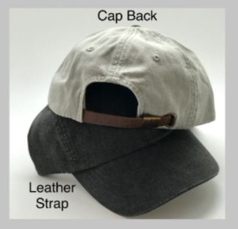 May include: A gray and black baseball cap with a leather strap and a metal buckle. The back of the cap says "Cap Back" and the strap says "Leather Strap".