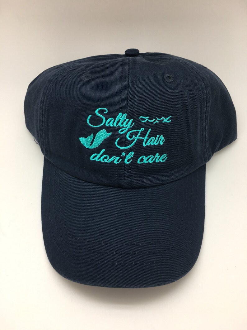 May include: A navy blue baseball cap with the text "Salty Hair don't care" embroidered in turquoise.