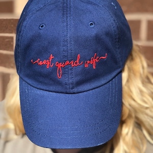 May include: A navy blue baseball cap with red embroidered text that reads "coast guard wife".