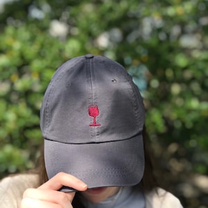 May include: A dark gray baseball cap with a red wine glass embroidered on the front.