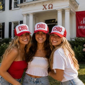 May include: Three matching trucker caps with white front panels and red mesh backs. Each cap features the word CHIO printed in bold red capital letters on the front. The caps have a structured crown and a red brim, designed with a snapback closure.
