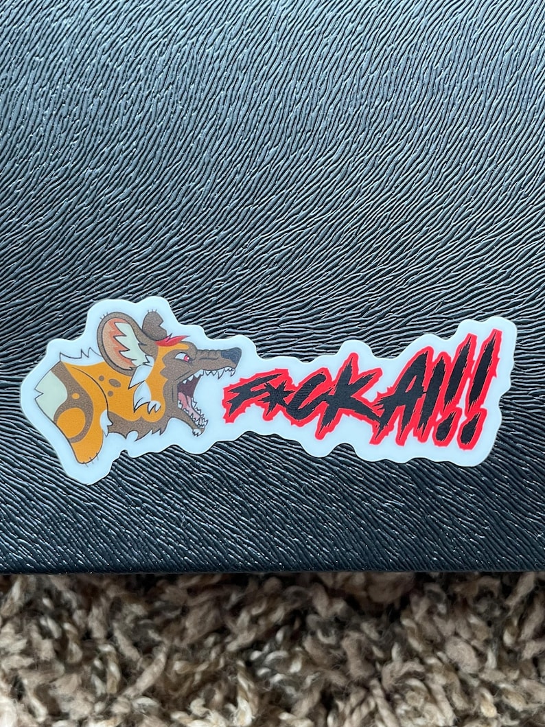 May include: A sticker featuring a cartoon African wild dog with an open mouth and the text "F*CK ALL!!!" in red and black. The sticker is on a textured black surface.