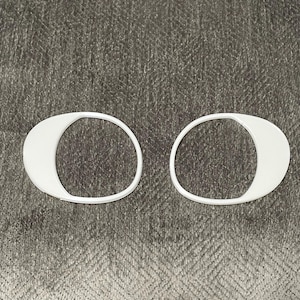 May include: Two white plastic oval-shaped rings. The rings are on a gray textured surface.