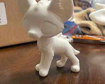 Puede incluir: Figurita de perro estilizado en 3D impreso en blanco con orejas grandes. La figurita está de pie sobre una superficie de madera.