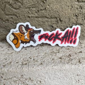 May include: A white sticker with a cartoon African wild dog in brown, tan, and black. The sticker has the red text "F*CK A!!". The dog is baring its teeth, and the sticker is on a textured surface.