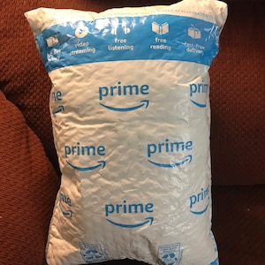 May include: White and blue Amazon Prime shipping package. The package features the word "prime" repeated, alongside icons for video streaming, free listening, free reading, and fast free delivery.