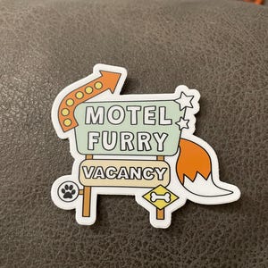 sticker cut into the shape of a motel sign with arrow, stars and tail attached. text reads motel furry — vacancy with a paw print and bone symbol underneath.