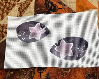 May include: A white Aida cloth with two purple and black outlined shapes with a pink star in the center of each shape.